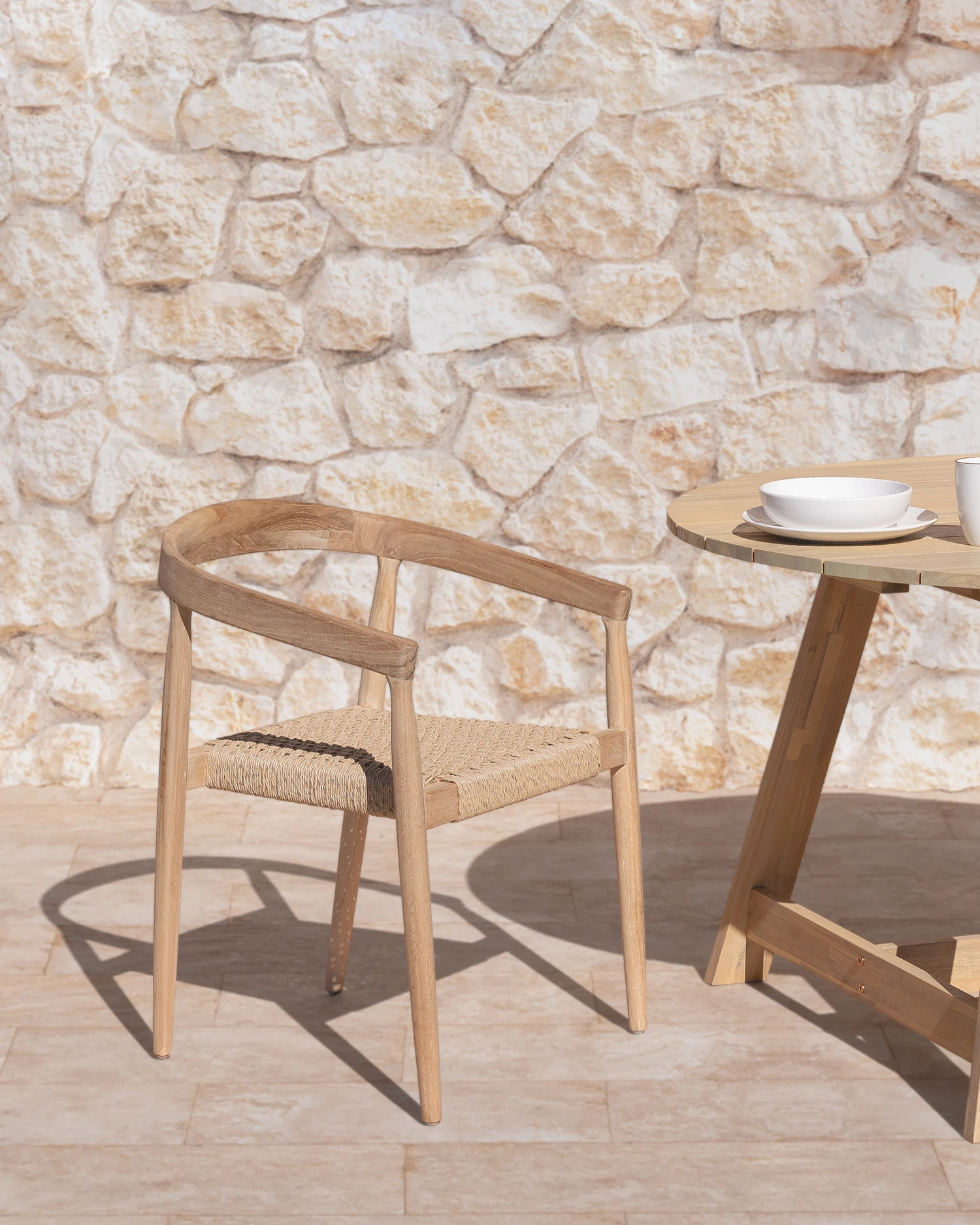 Silla de jardín con respaldo de madera y asiento en cuerda beige expuesta en exterior con pared de piedra