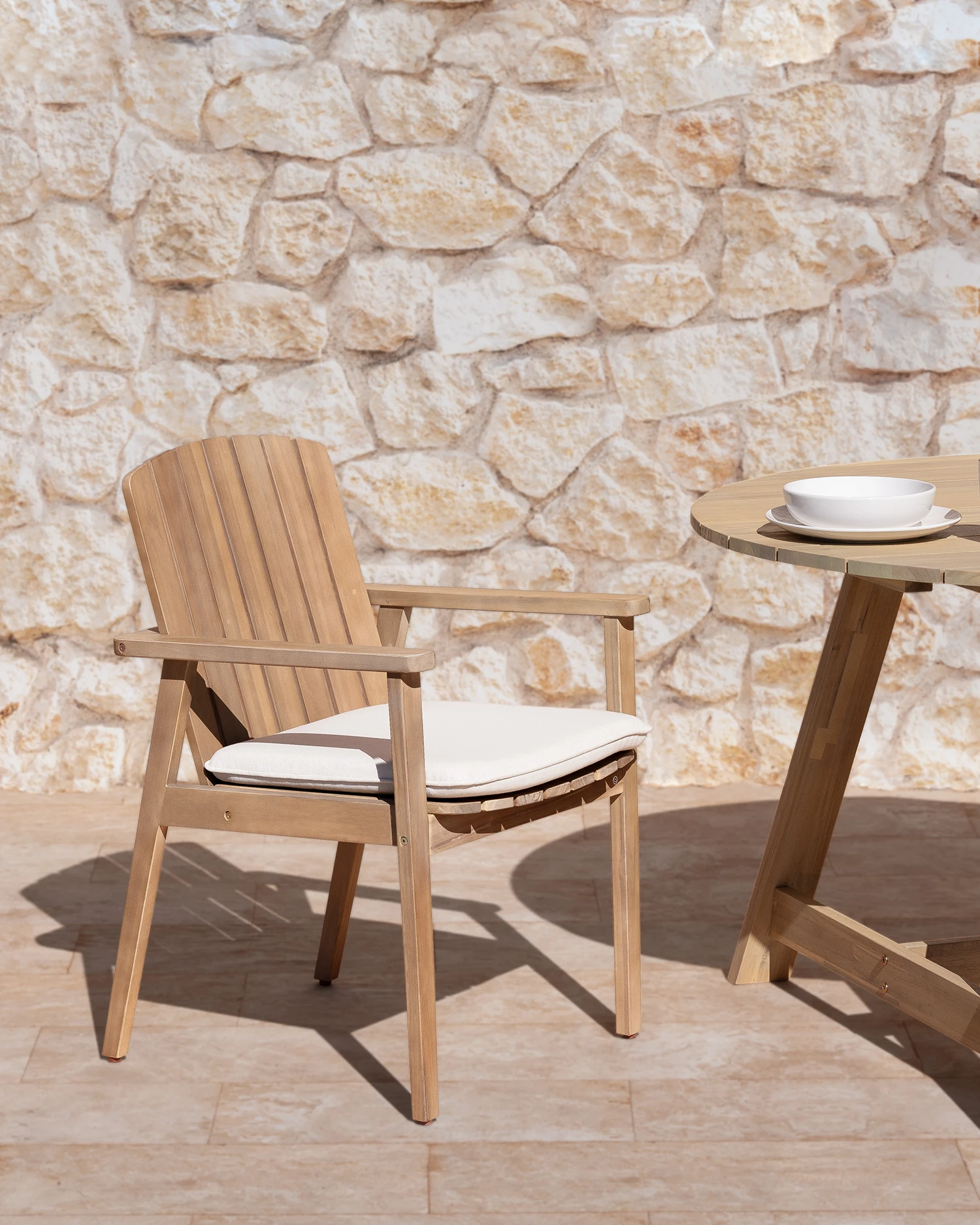 Chaise de jardin en teck et rotin synthétique exposée à l’extérieur avec paroi en pierre