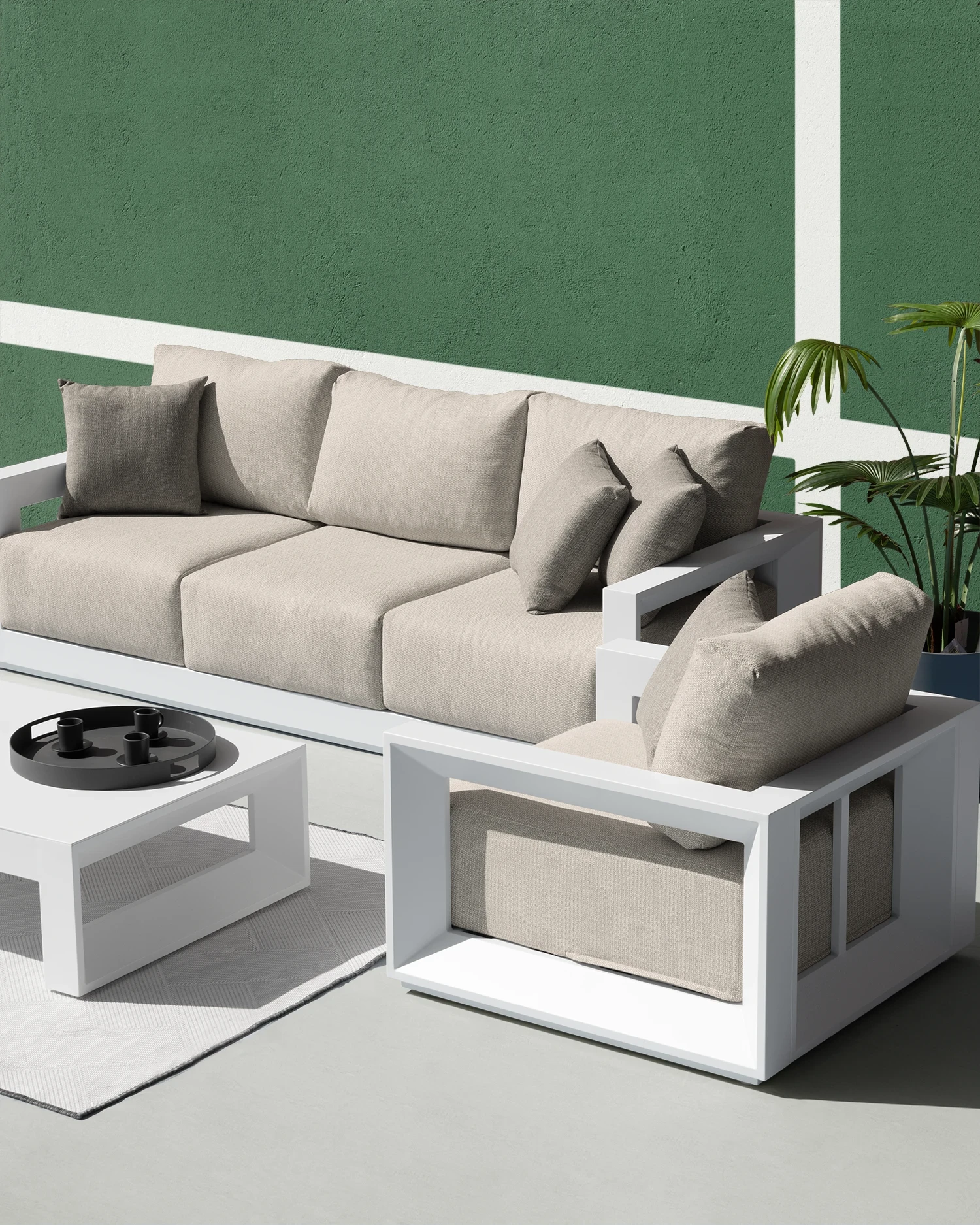 White side table and sofas with pearl grey textiles, arranged in an outdoor space with a green wall