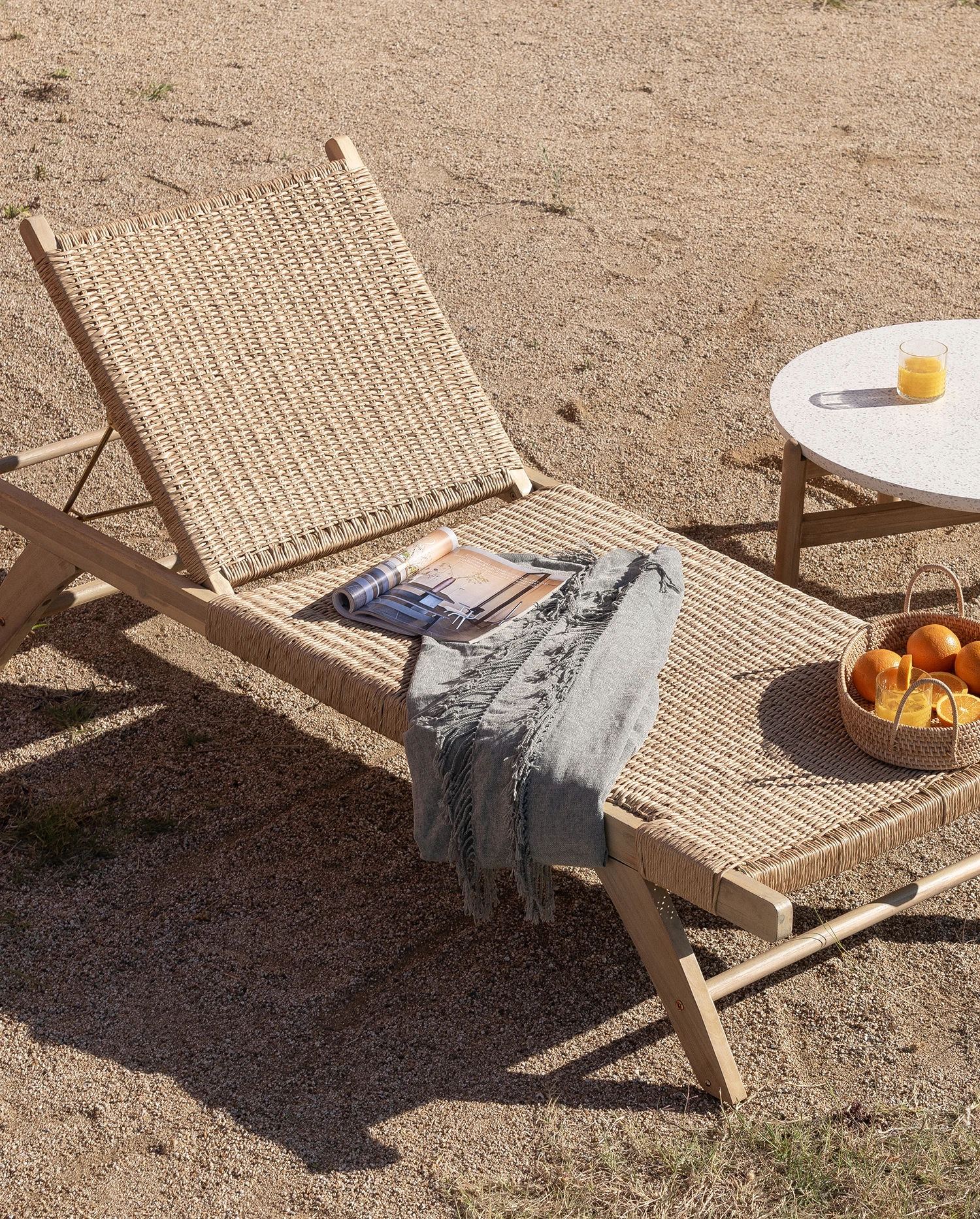 Chaise longue et table d’appoint contenant quelques jus d’orange, un bol de fruits avec des oranges et un magazine